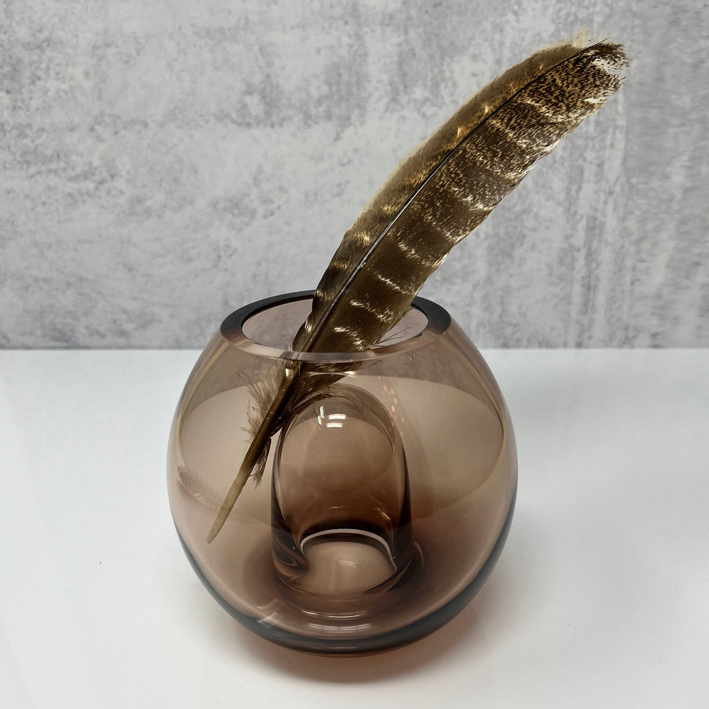 A brown glass vase with a feather in it created by House of Good.