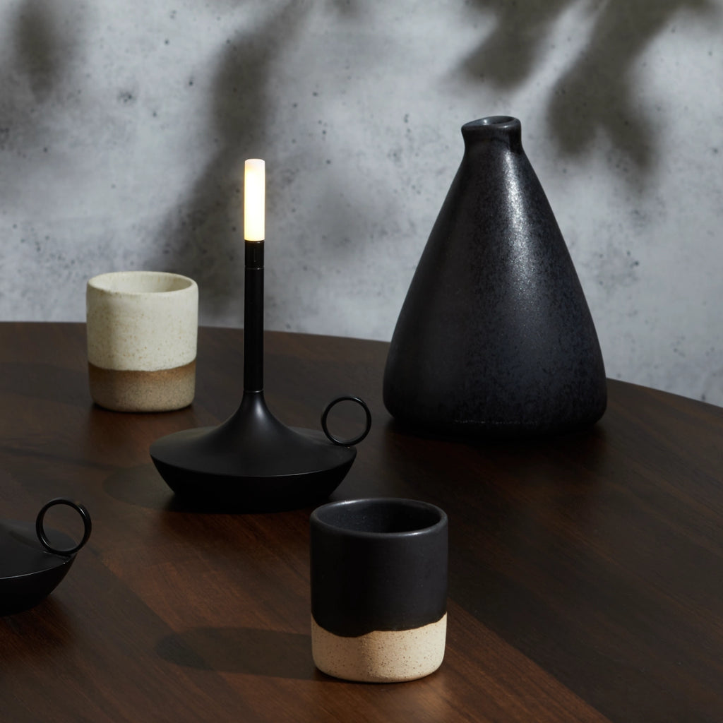 A table with vases, a GRAYPANTS WICK PORTABLE LAMP, and a rechargable candle for creating ambiance.