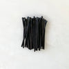 A bunch of handmade black match sticks from House of Good wooden matchbox on a white surface.