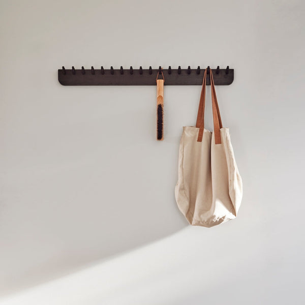 A wooden bench with an ECHO COAT RACK 88 hanging on it, perfect for hallway essentials or as a coat rack. This stylish piece, designed by FORM & REFINE, adds both functionality and elegance to any space.