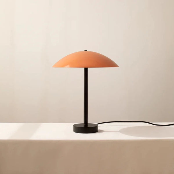 The Arundel Table Lamp, with its stunning aesthetics, adds a touch of innovation to any space. This eye-catching orange lamp from IN COMMON WITH sits beautifully on a white table, creating a striking visual.