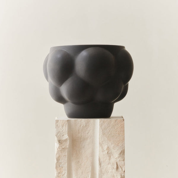 A black Ceramic Balloon Bowl 06, reminiscent of Louise Roe's design aesthetic, sitting on top of a stone pedestal.