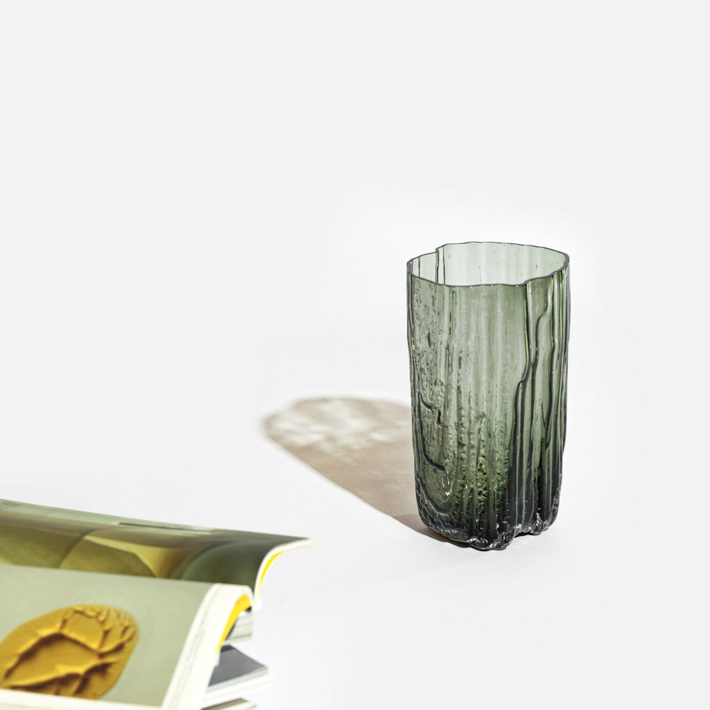A MELT VASE from ANTREI HARTIKAINEN with a smooth texture is placed on a table beside a book.