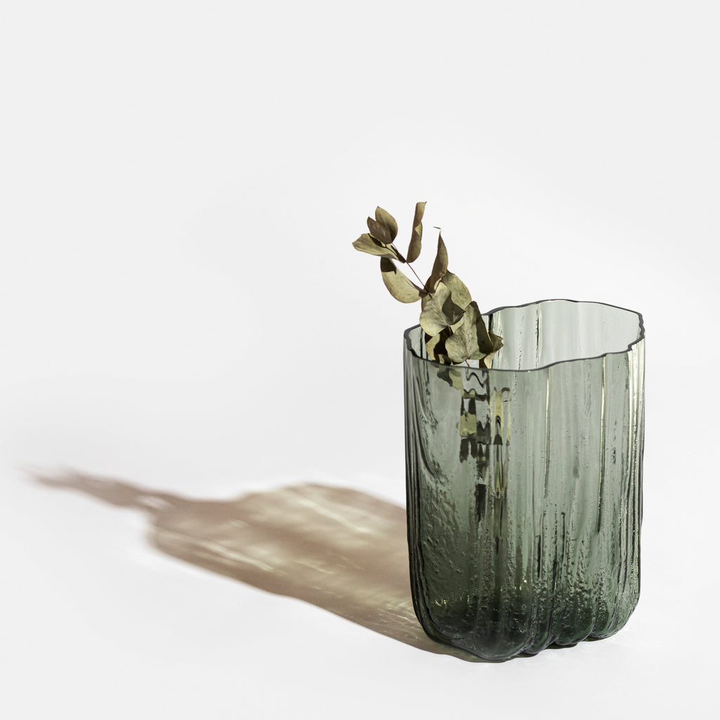 A green MELT VASE by ANTREI HARTIKAINEN with a single flower in it, perfect for your vase collection.