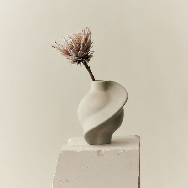 An organic design of the PIROUT VASE VINTAGE GLAZE by LOUISE ROE featuring a flower delicately placed on top.