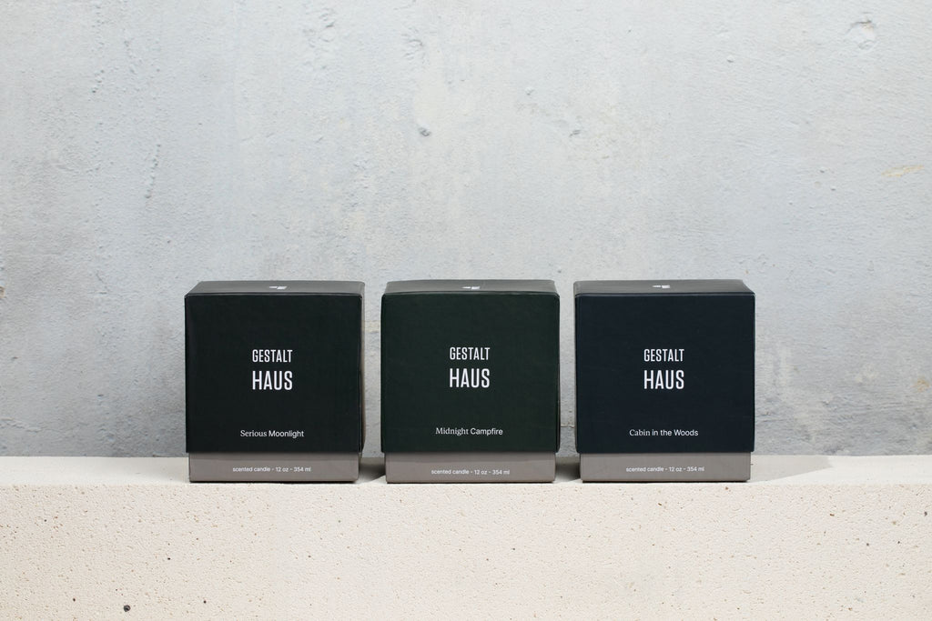 Three boxes of CABIN IN THE WOODS CANDLE from GESTALT HAUS on a concrete slab with a hint of moss.