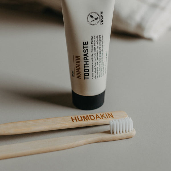 A tube of HUMDAKIN toothpaste vegan + fluoride free and a toothbrush promoting dental hygiene.