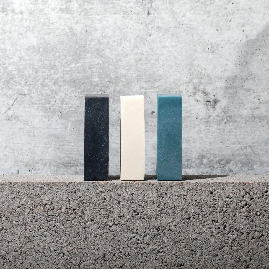 Three Gestalt Haus activated charcoal bar soap bars sitting on top of a concrete wall.