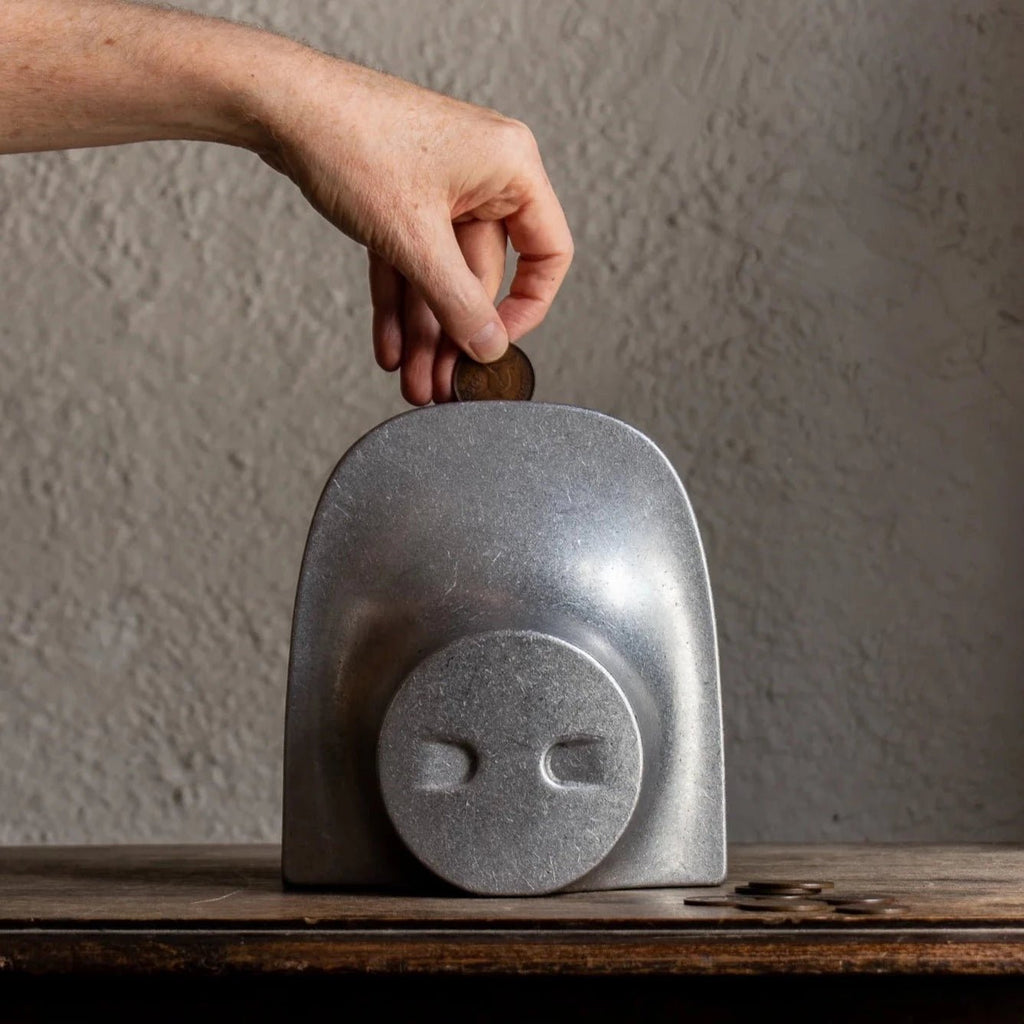 A person inserting a COINK into a metal piggy bank bookend by STUDIO HENRY WILSON.