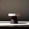 A small table with a black base on a white COLISEU PEDESTALS by ORIGIN MADE.