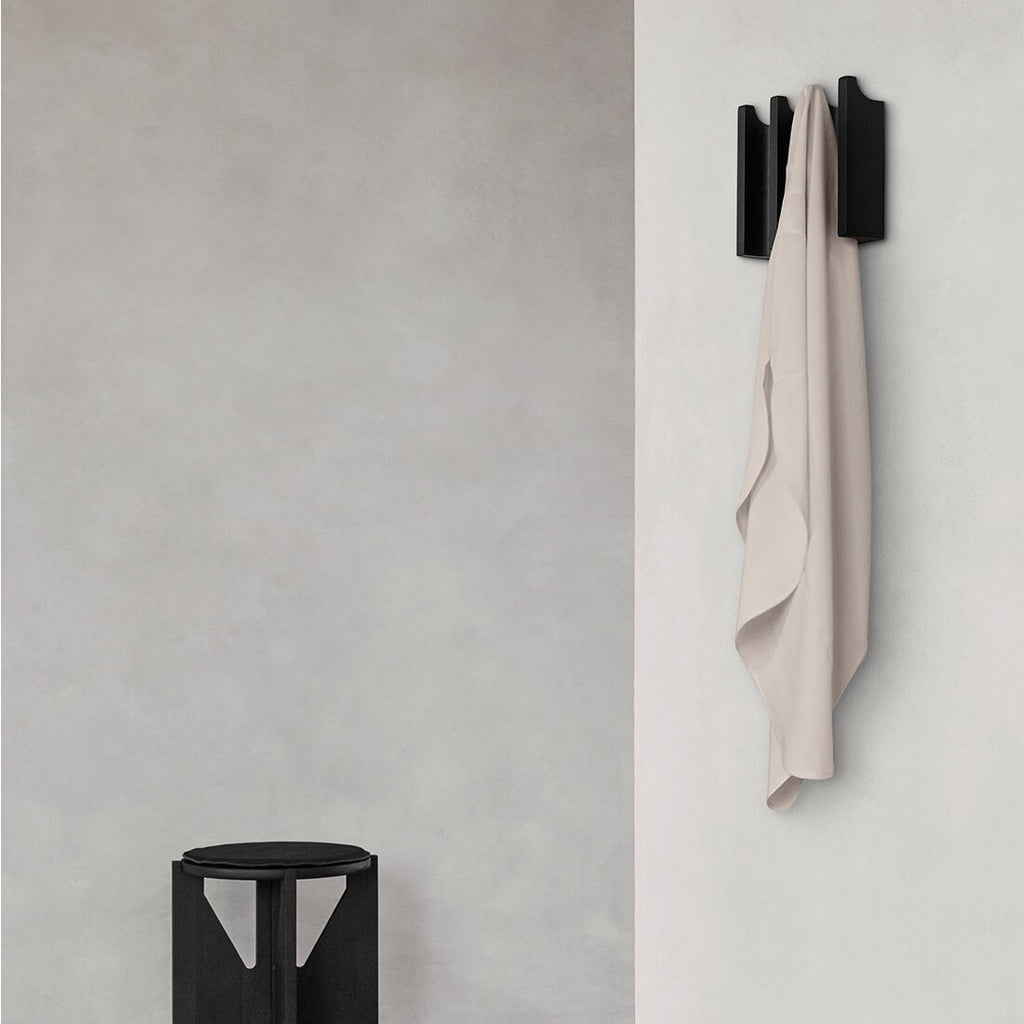 A COLUMN COAT RACK designed by KRISTINA DAM STUDIO hanging on a wall next to a stool.