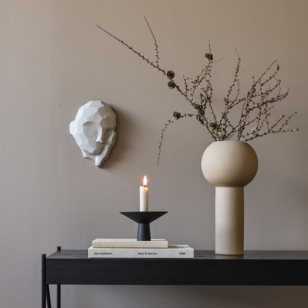 A DREAMER SCULPTURE by COOEE with a candle on a table next to a Gestalt Haus wall.