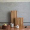 A FRAMA DRY STUDIOS OAK CUTTING BOARD on a counter next to a bowl of apples.