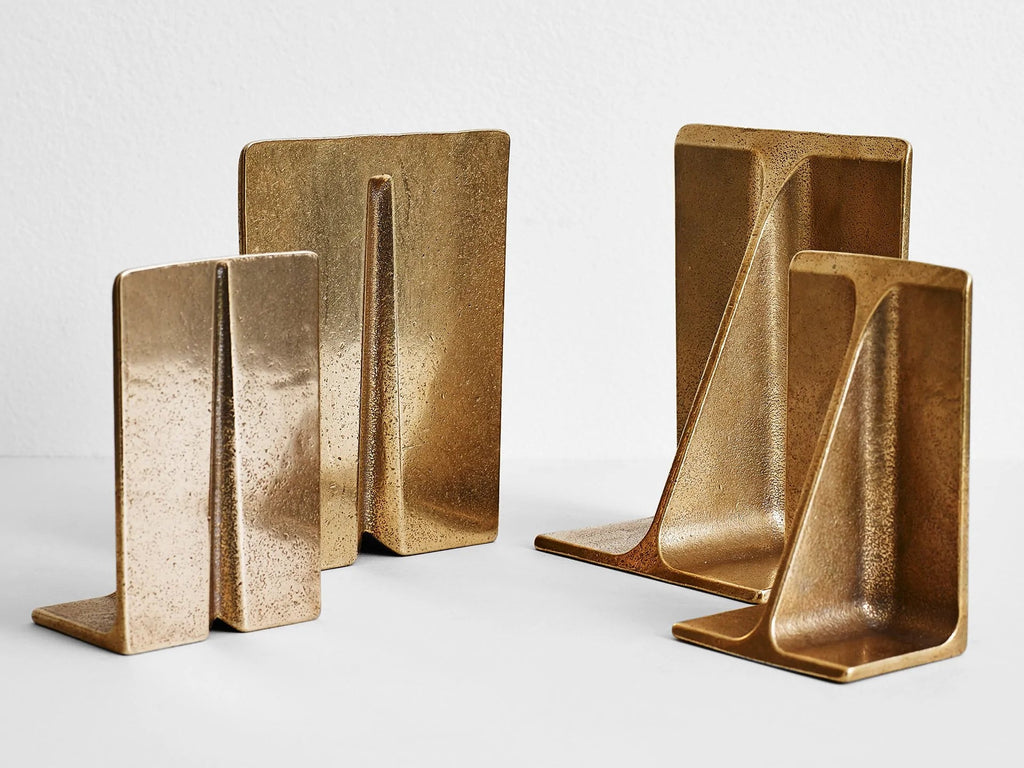Three brass bookends by STUDIO HENRY WILSON on a white surface.