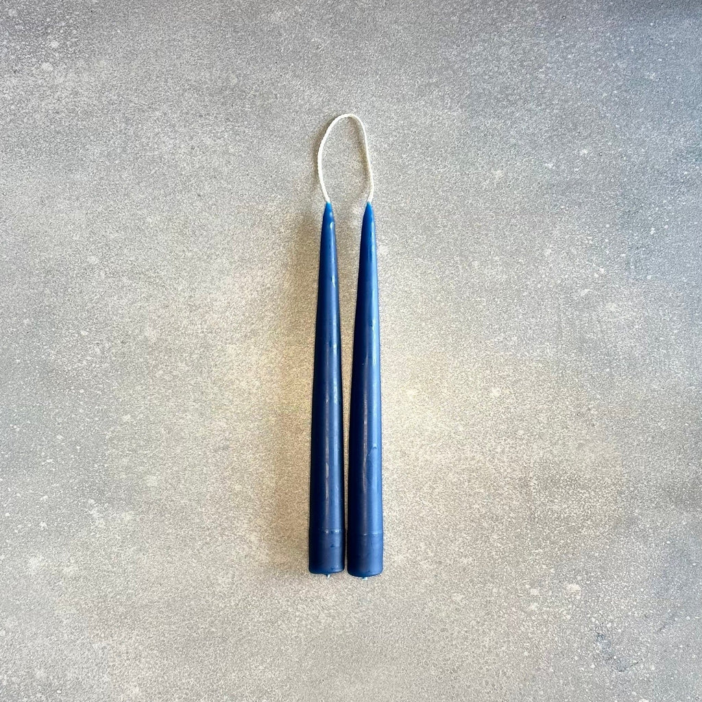 A pair of HAND-DIPPED TAPER CANDLES on a concrete surface, designed by DANICA DESIGNS.