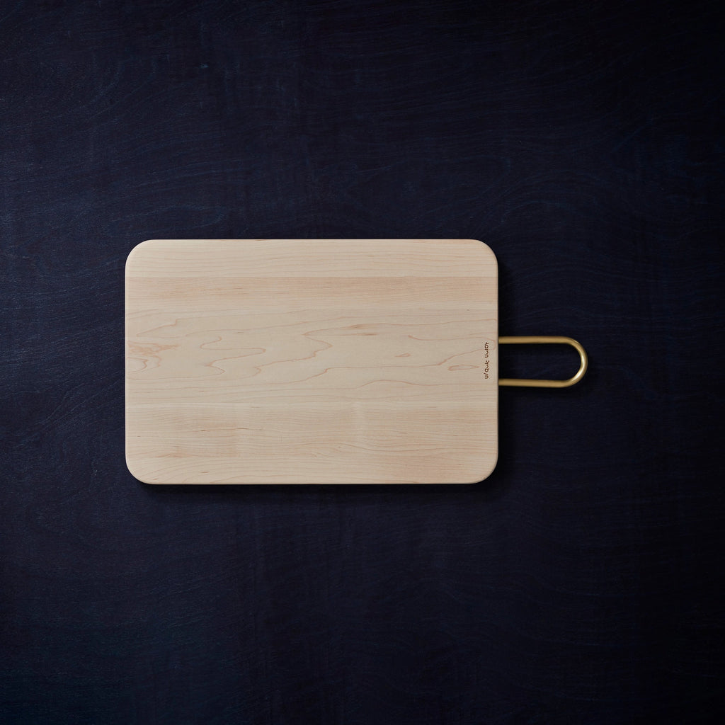 An AARON PROBYN HEATH MAPLE CUTTING BOARD with a golden handle sold at Gestalt Haus.