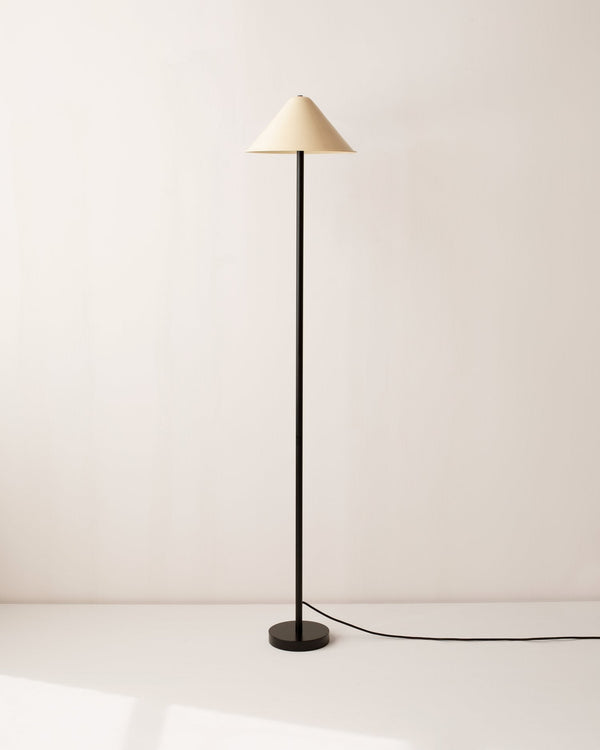 An In Common With Eave floor lamp with a beige shade on a white floor.
