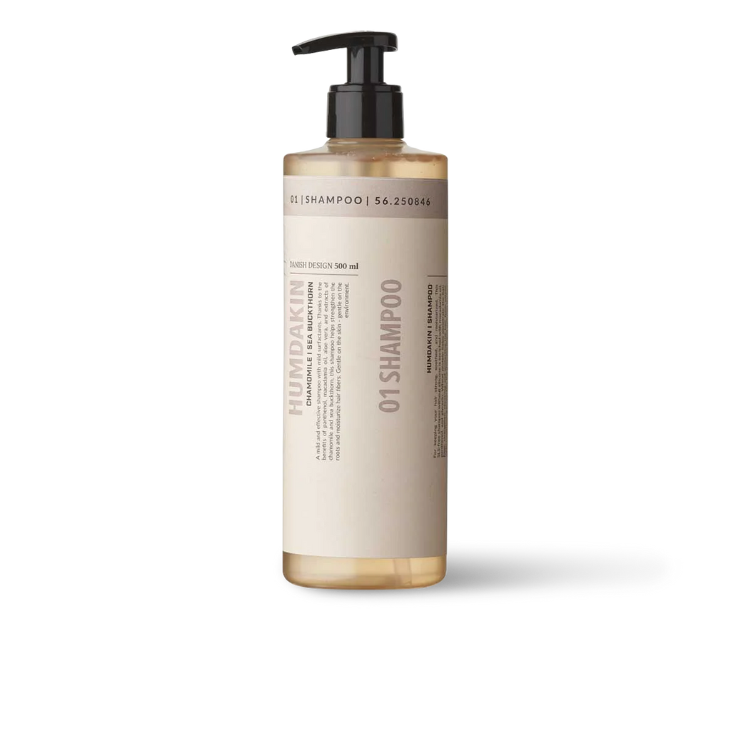A bottle of 01 SHAMPOO SEA BUCKTHORN + CHAMOMILE by HUMDAKIN on a white background with chamomile.