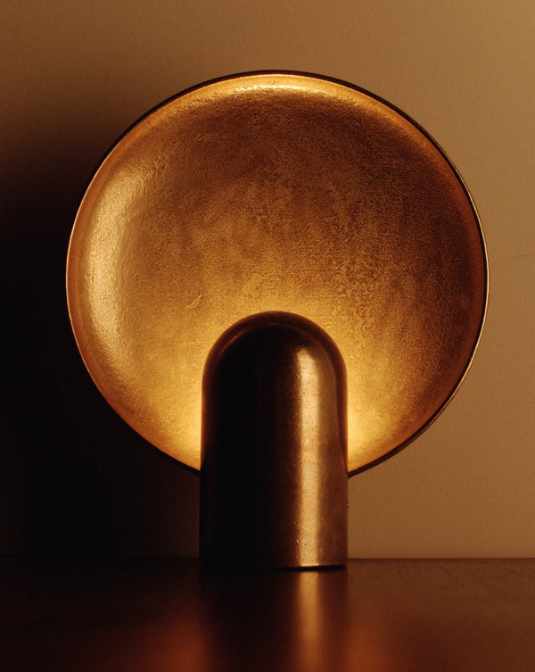 A STUDIO HENRY WILSON SURFACE SCONCE BRASS on a table in an ambient, dark room.