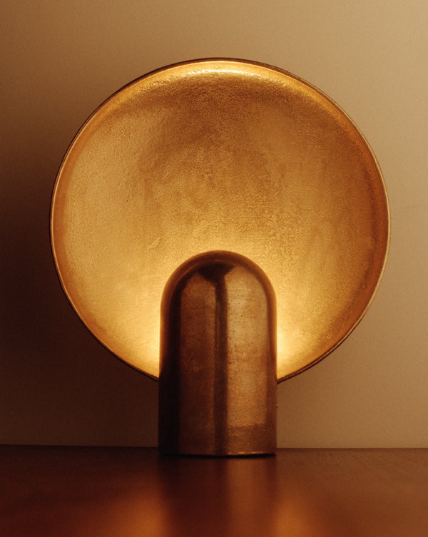 A STUDIO HENRY WILSON SURFACE SCONCE BRASS on a wooden table, creating an ambient glow.