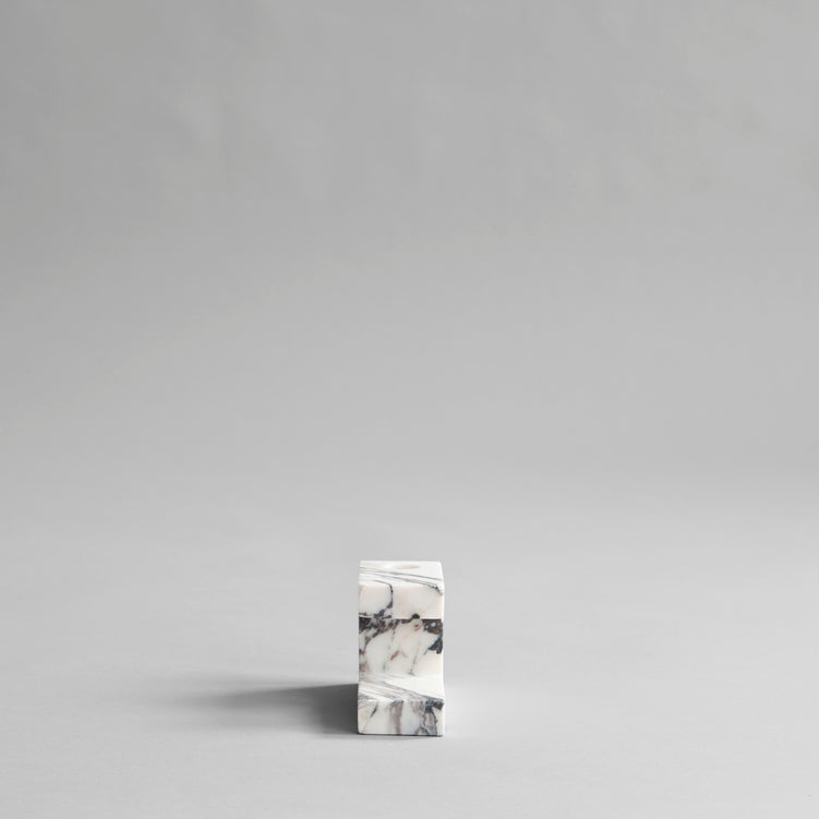 A small solid BRICK CANDLE HOLDER in a geometric shape sitting on top of a grey surface, made by 101 COPENHAGEN.
