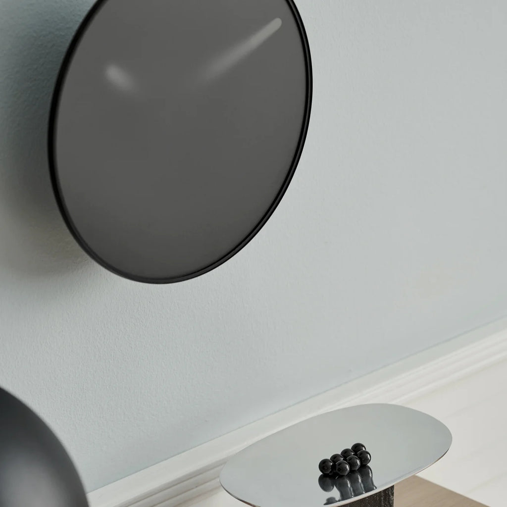 A MOMENTT WALL CLOCK by GEJST, a minimalist black wall clock, hanging next to a table.