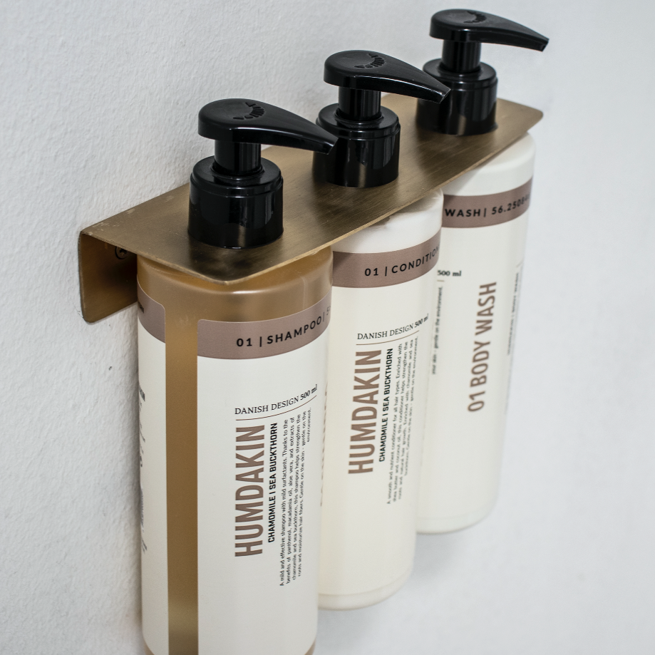 Three Humdakin Bottle Hanger Triples of shampoo hanging on a wall.