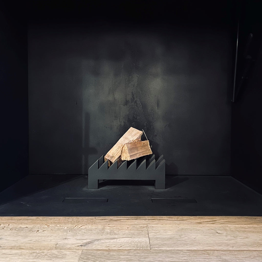 A black fireplace with logs in it showcasing architectural ingenuity, featuring the FIREDOG FIRE IRONS BY JEAN-MICHEL WILMOTTE from WHEN OBJECTS WORK.