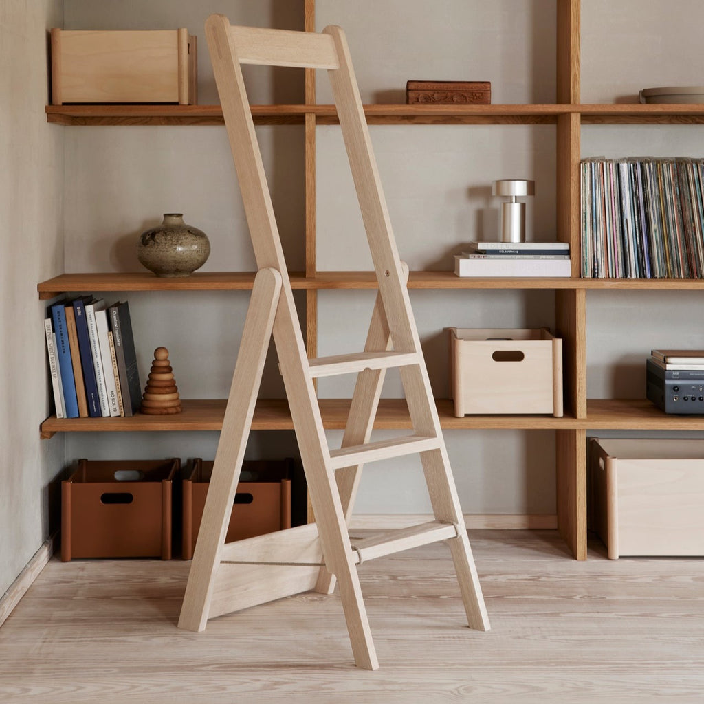 A FORM & REFINE STEP BY STEP LADDER, both foldable and a decorative object, in a room with bookshelves.