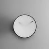A minimalist black and white photo of a GEJST MOMENTT WALL CLOCK made of steel.