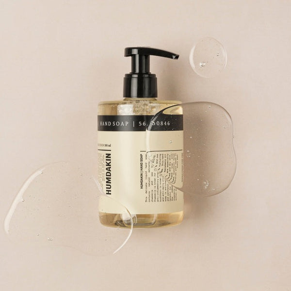 A bottle of HUMDAKIN 05 HAND SOAP RHUBARB + BIRCH featuring the invigorating scent of rhubarb and birch, resting on a beige surface.