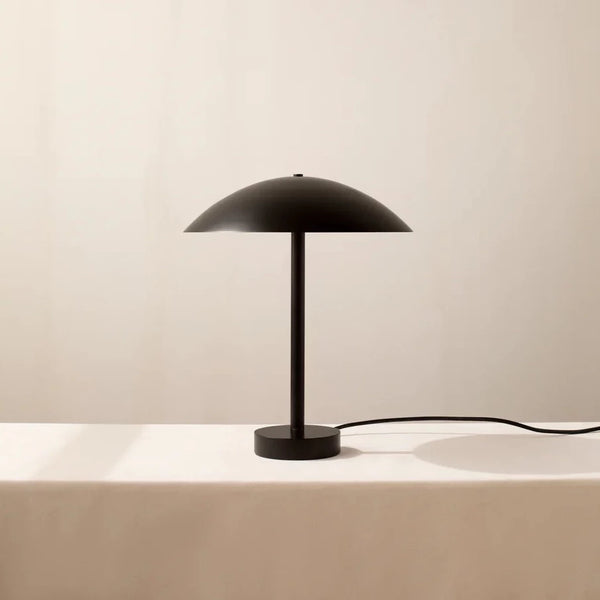 The IN COMMON WITH Arundel Table Lamp showcases innovation and aesthetics, with its sleek design featuring a black lampshade perched on a white table.