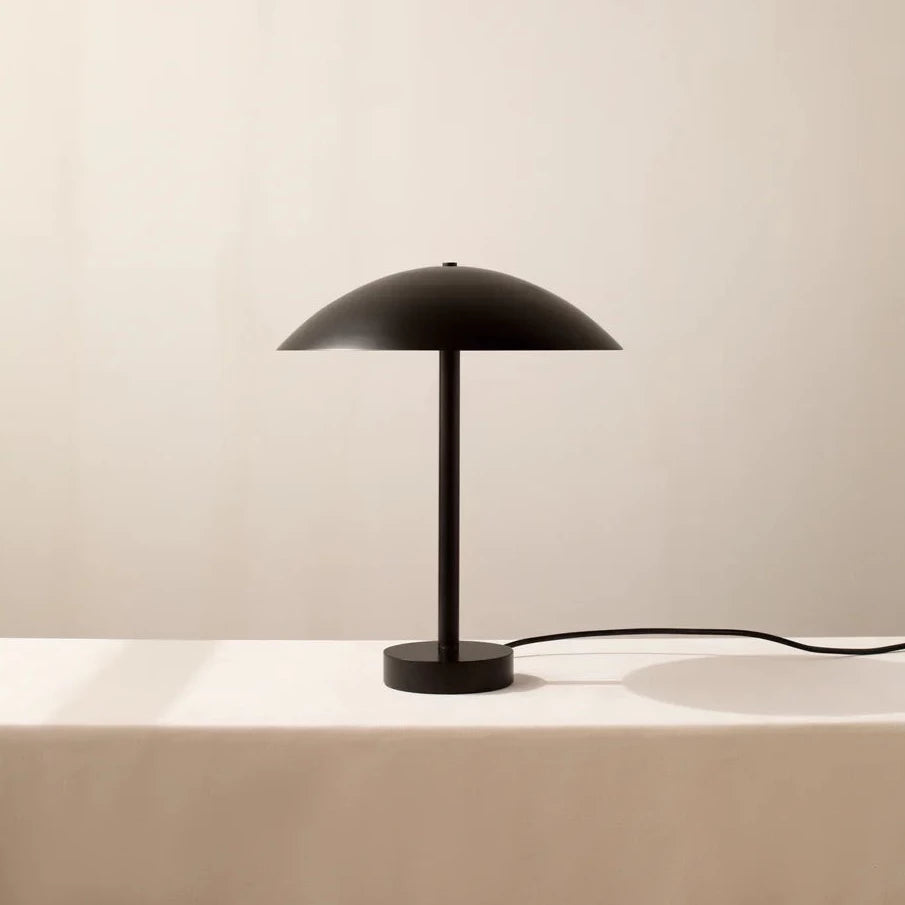 The IN COMMON WITH Arundel Table Lamp showcases innovation and aesthetics, with its sleek design featuring a black lampshade perched on a white table.