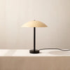 The Arundel Table Lamp, by In Common With, featuring stunning aesthetics and innovative design, provides a soft and comforting glow on a sleek white table.