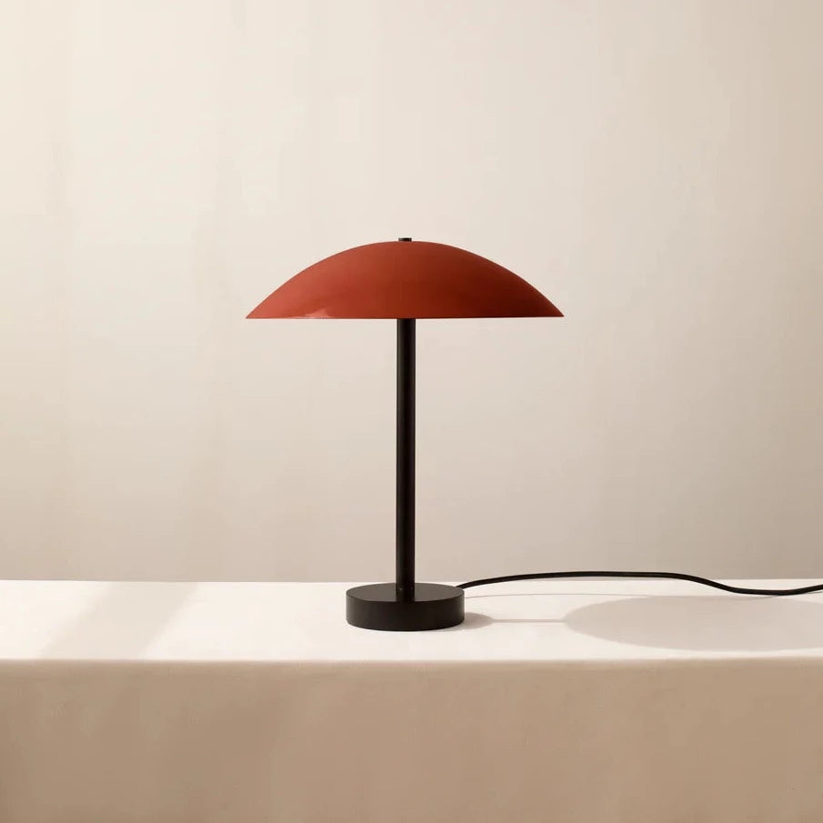 The ARUNDEL Low Table Lamp by IN COMMON WITH brings innovation to any space with its striking aesthetics, featuring a red lamp situated on a sleek white table.