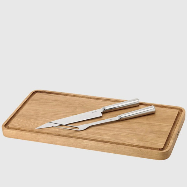 A STELTON wooden cutting board with SIXTUS CARVING FORK stainless steel grill utensils on it.