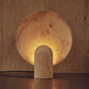 A SURFACE SCONCE CLASSICO TRAVERTINE lamp by STUDIO HENRY WILSON providing ambient light on a table.