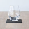 A clear wine glass sitting on a Lind DNA Square Glass Mat made from recycled leather.