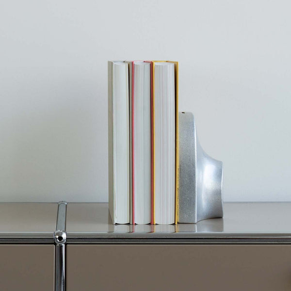 A stack of COINK PIGGY BANK BOOKEND books on top of a metal shelf at STUDIO HENRY WILSON, surrounded by the atmosphere of Gestalt Haus.