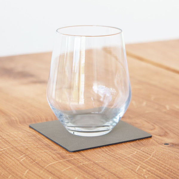 A wine glass on a Square Glass Mat, made from Lind DNA's recycled leather, resting on a wooden table.