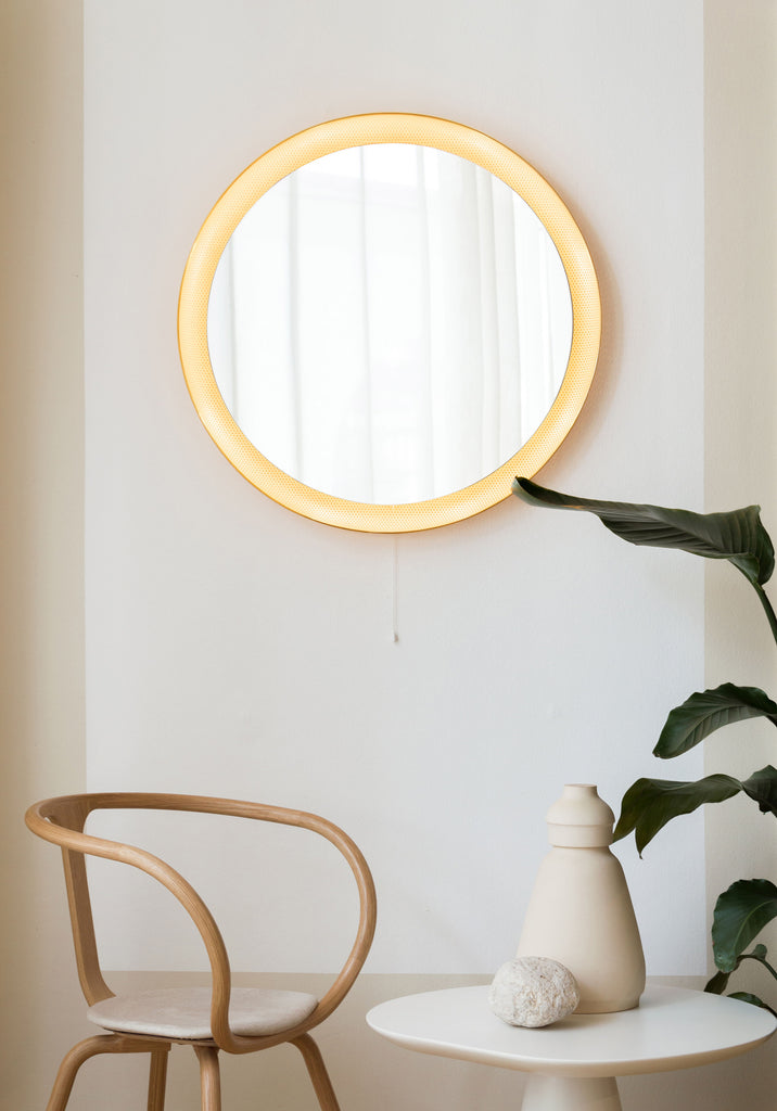 An ATBO Floris Wall Mirror hangs on a wall next to a chair and a plant.