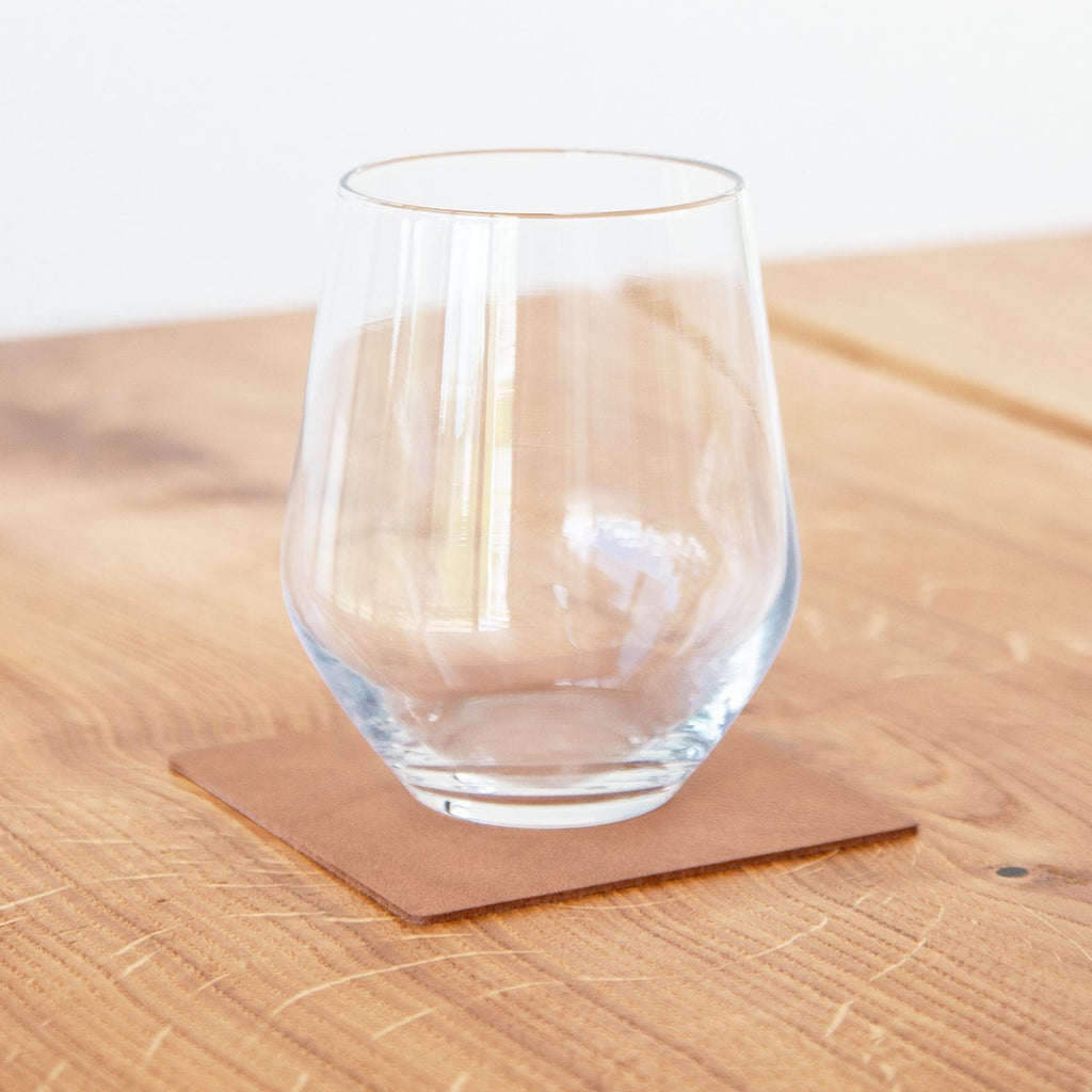 A wine glass on a wooden table with a Square Glass Mat made from recycled leather, featuring Lind DNA as the SEO keywords.