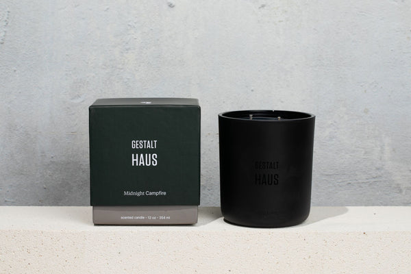 A MIDNIGHT CAMPFIRE CANDLE by GESTALT HAUS, with a box next to it, emitting the tantalizing scent of smoked wood.