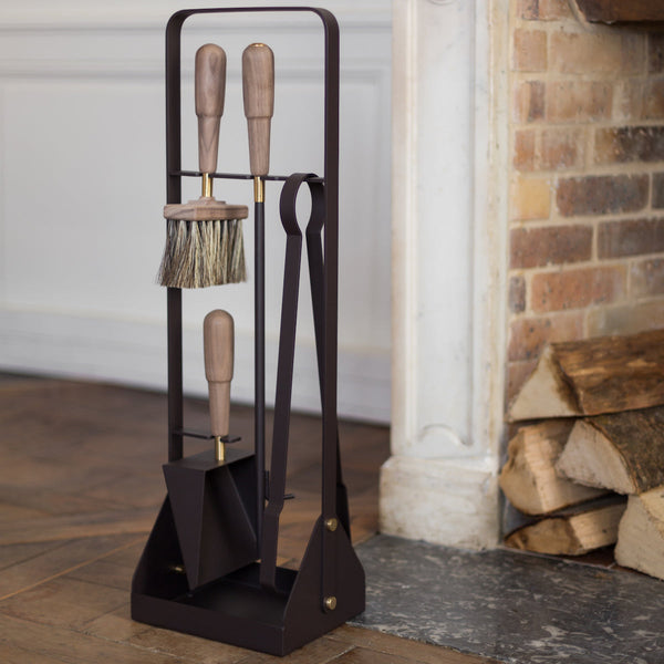 An EMMA FIRE TOOL COMPANION SET by ELDVARM on a stand in front of a fireplace.
