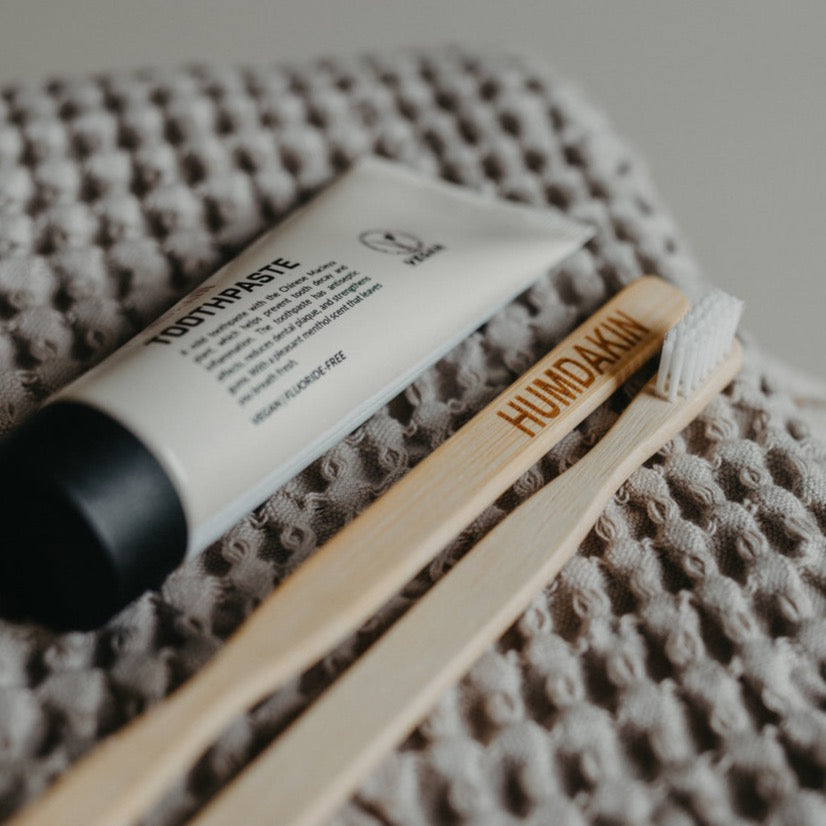 A sustainable source ORGANIC BAMBOO TOOTHBRUSH by HUMDAKIN and a tube of organic toothpaste on a blanket.