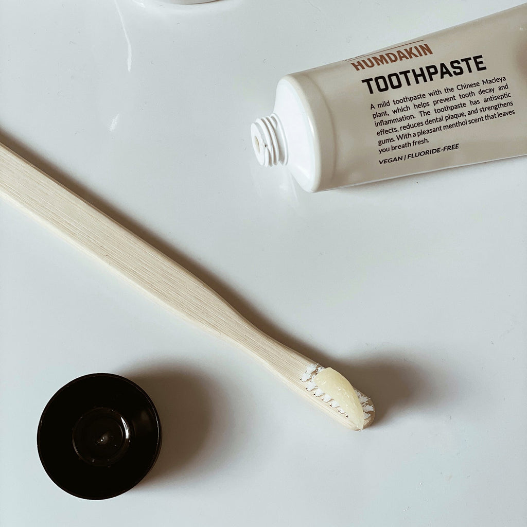 A HUMDAKIN ORGANIC BAMBOO TOOTHBRUSH and a tube of toothpaste on a white surface.