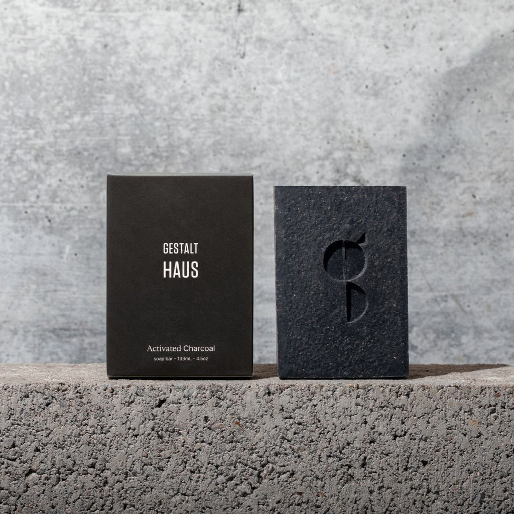 A Gestalt Haus activated charcoal bar soap showcased on a concrete wall.