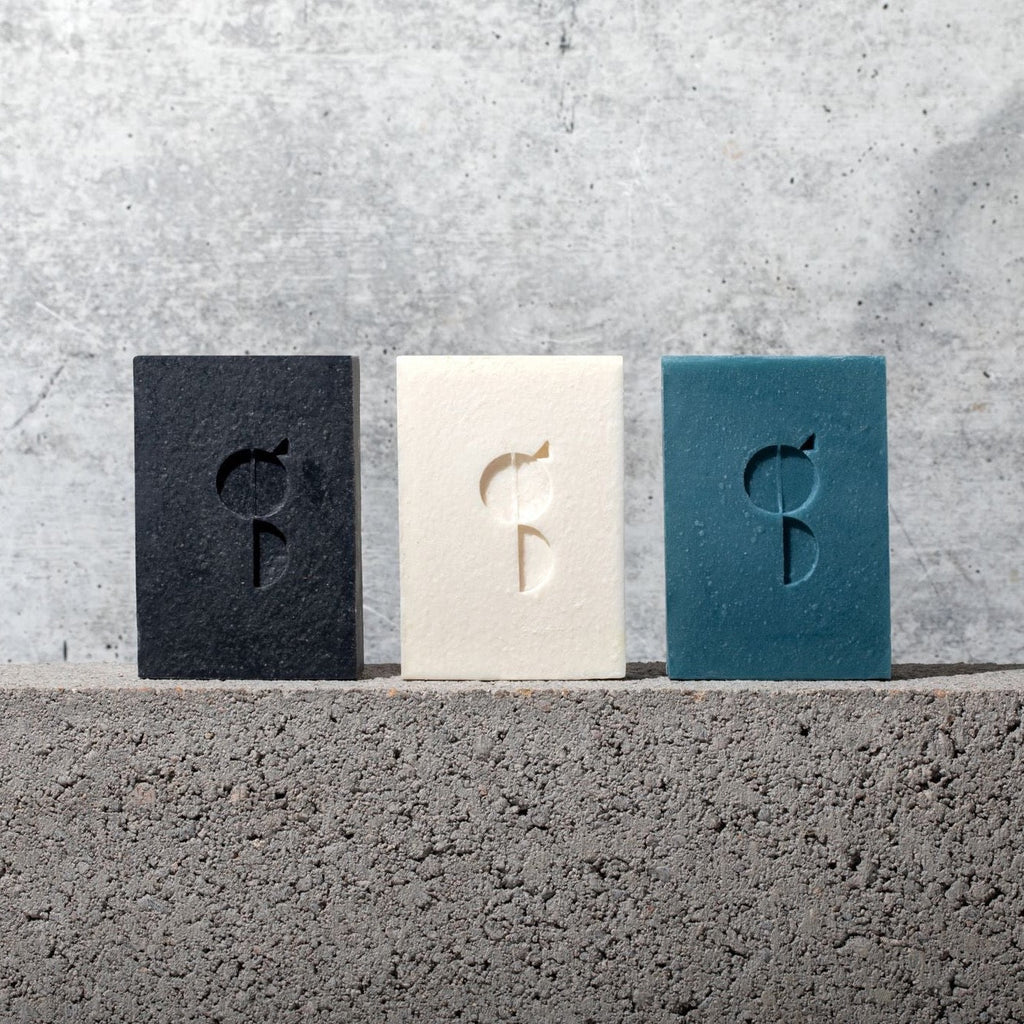 Three Gestalt Haus Activated Charcoal Bar Soaps sitting on top of a concrete wall.