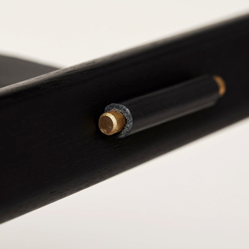 A close up of a black wooden ANGLE FOLDABLE STOOL with a brass knob by FORM & REFINE in the Gestalt Haus interior.