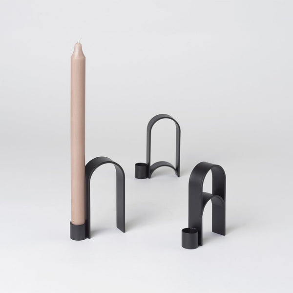 A black ARCH CANDLEHOLDER VOL. 2 with a beige candle by KRISTINA DAM STUDIO in the style of Gestalt Haus.